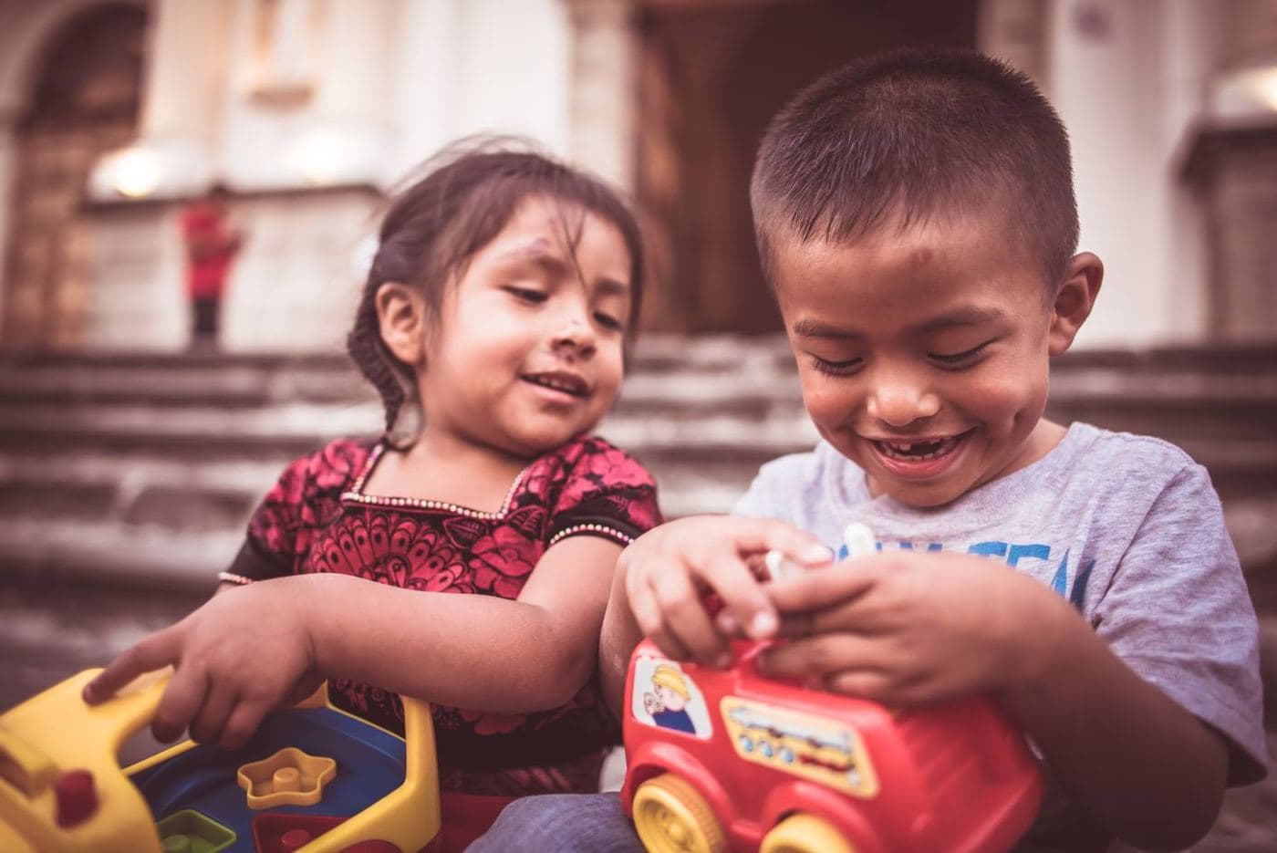 Two children laugh as they play with new toys on the steps of a church in Guatemala
