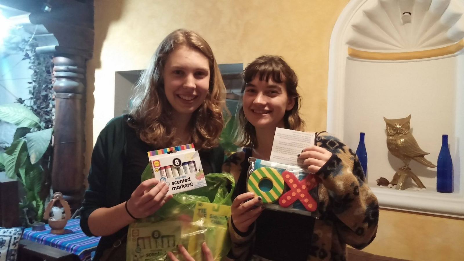 Two young donors hold up markers, sidewalk chalk and an X-and-O game in a room with yellow walls