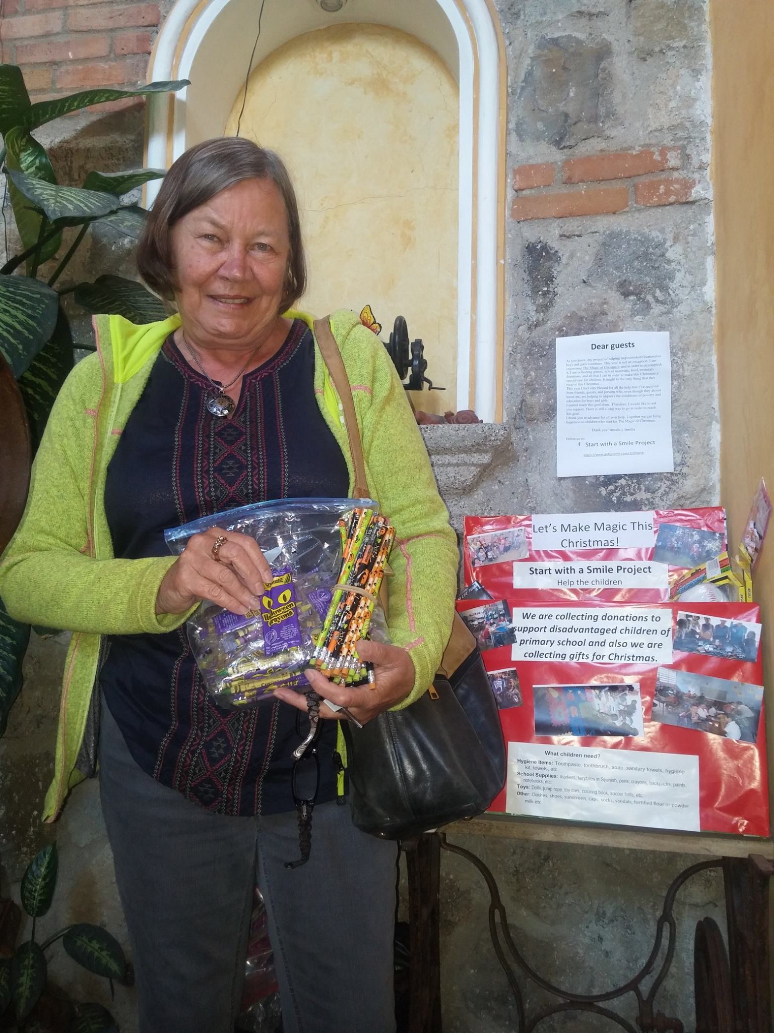 A donor smiles with crayons and pencils beside the project's red Christmas donation poster