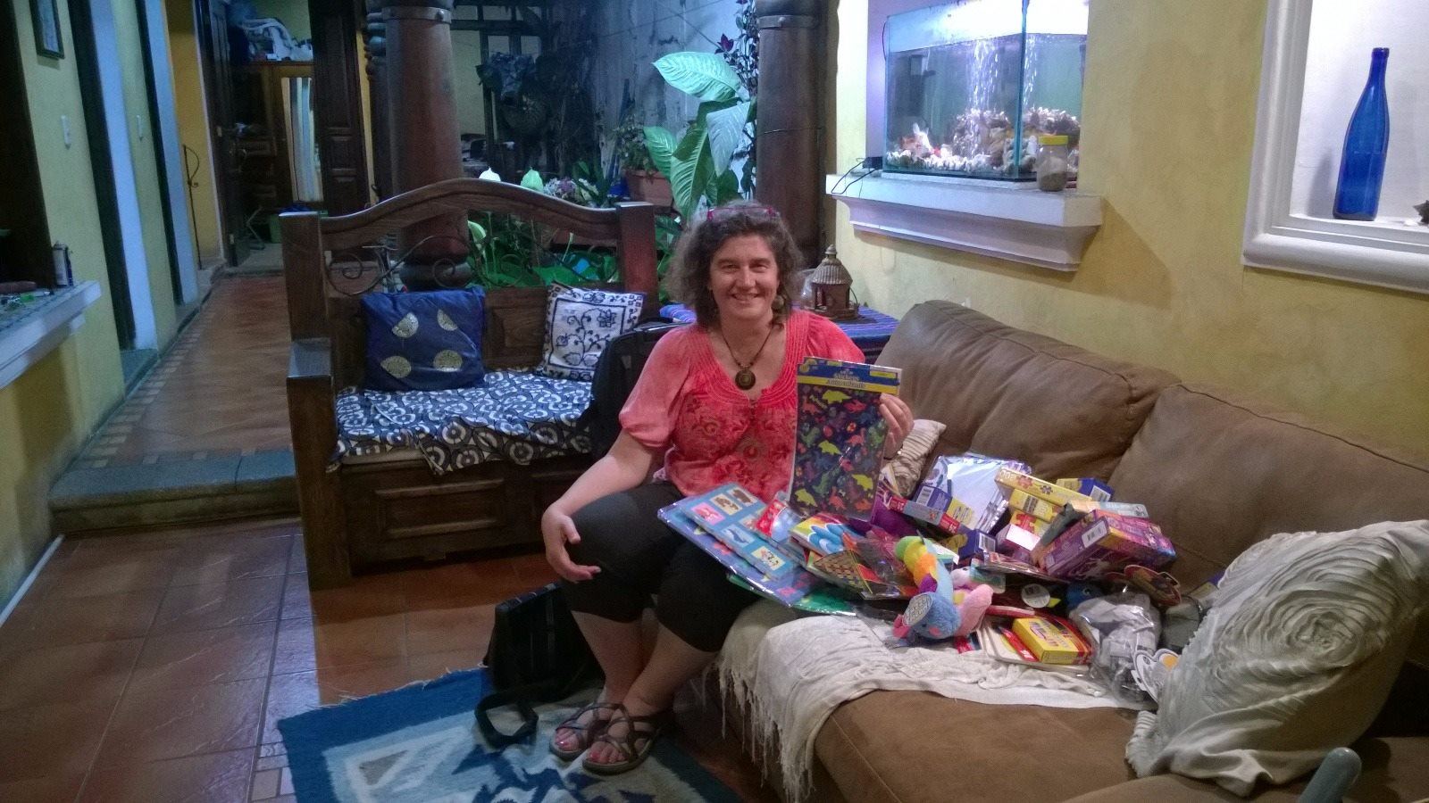 A donor on a sofa holds up dinosaur stickers beside a pile of toys and puzzles