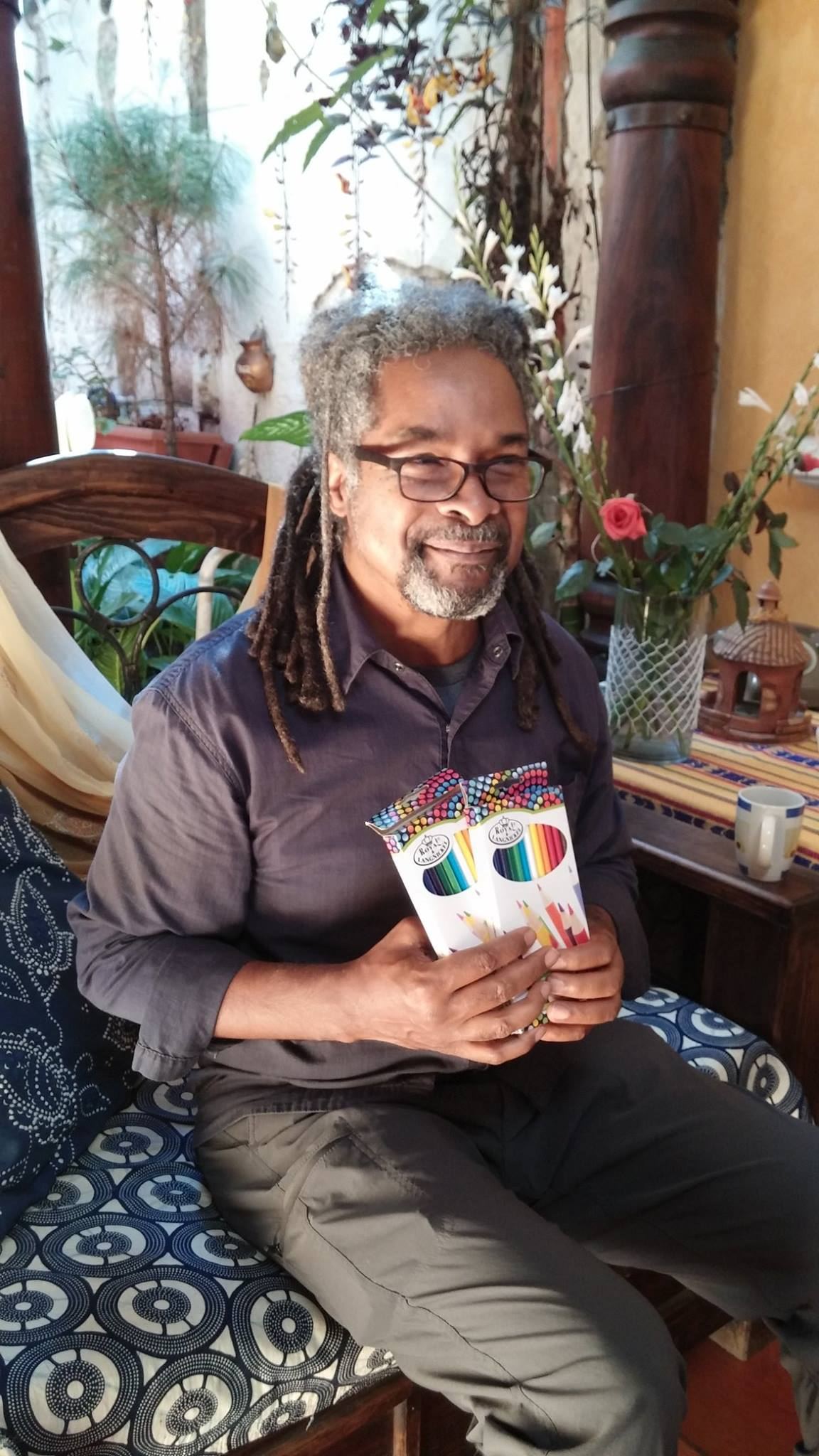 A smiling donor sits on a wooden bench holding two boxes of colored pencils