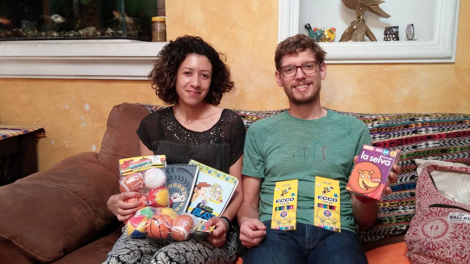 Two donors on a sofa show small balls, notebooks, colored pencils and a children's game