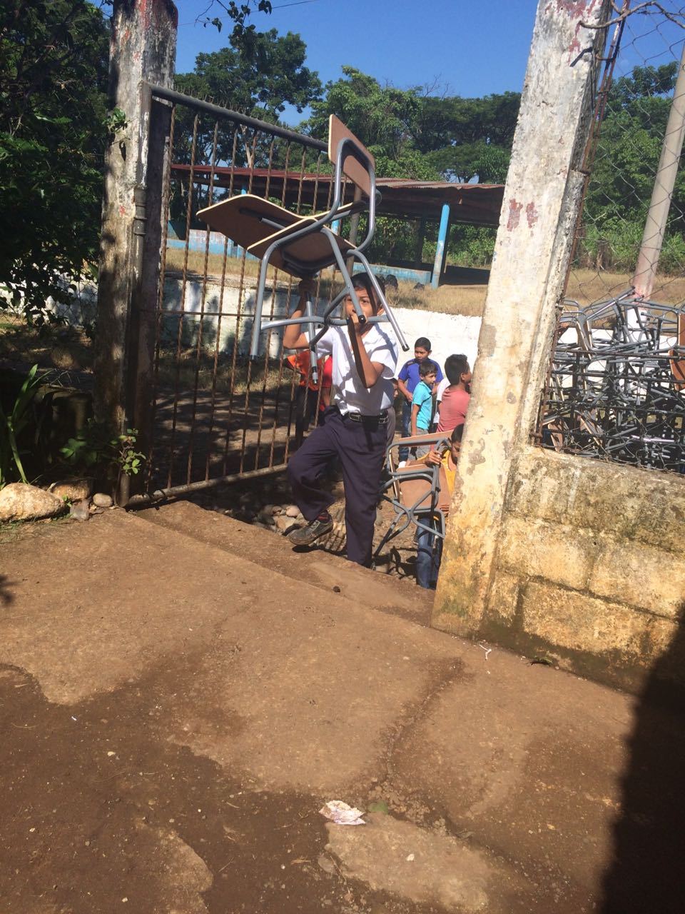A student walks through the gate of the Las Delicias school carrying a new desk on his head