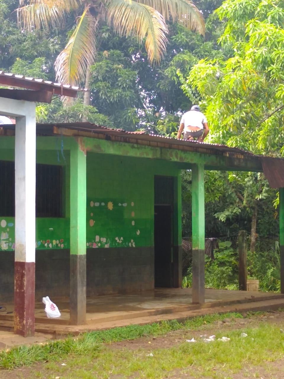 A man works crouched on the metal roof of a green classroom at the Las Delicias school
