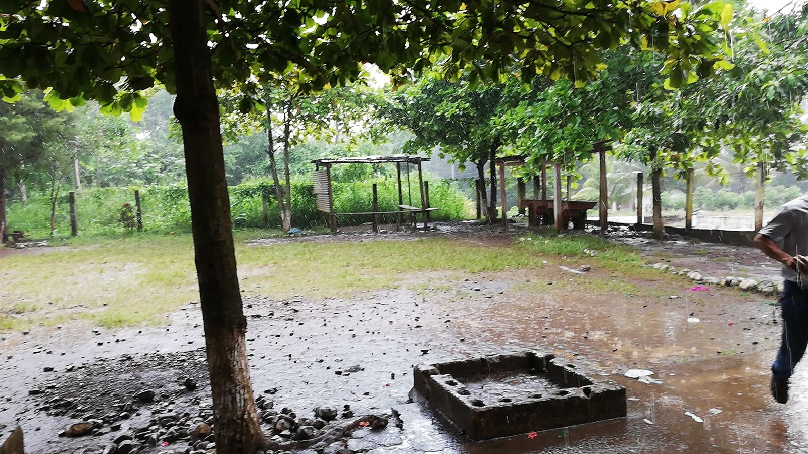 Heavy rain falls on the dirt courtyard of the Las Delicias school, with puddles and open shelters behind