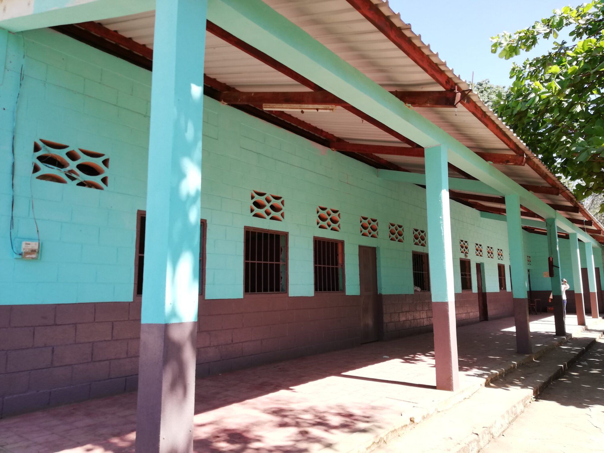 Freshly painted turquoise corridor of the Las Delicias school, with columns, decorative blocks and a metal roof