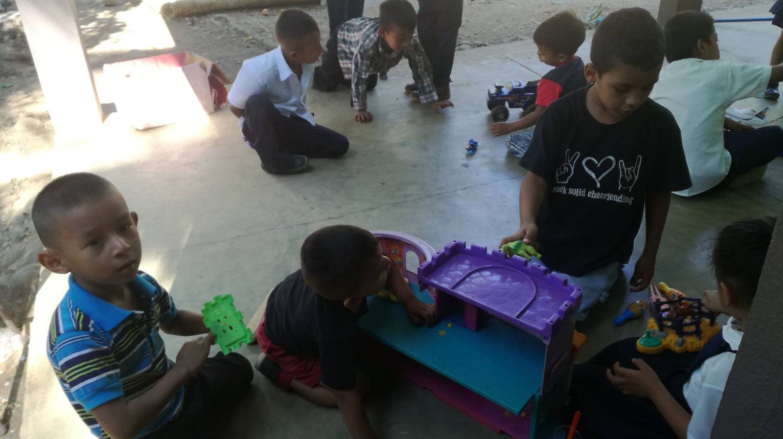 Boys play on a concrete corridor floor with a toy castle, toy trucks and building blocks