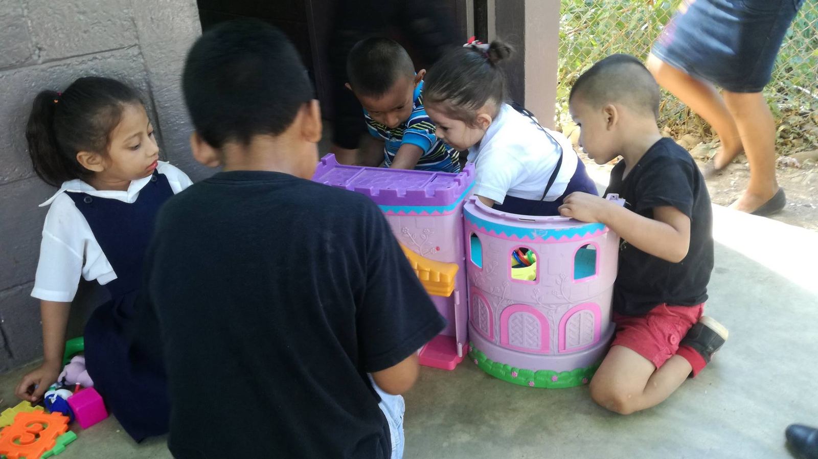 Young children play around a pink toy castle on a concrete floor