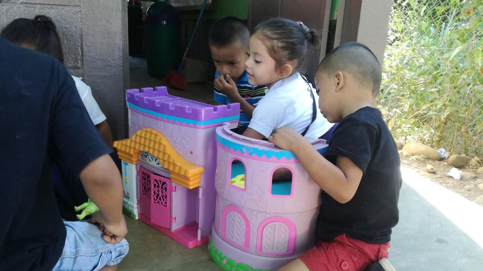 Three young children peek inside the tower of a pink toy castle