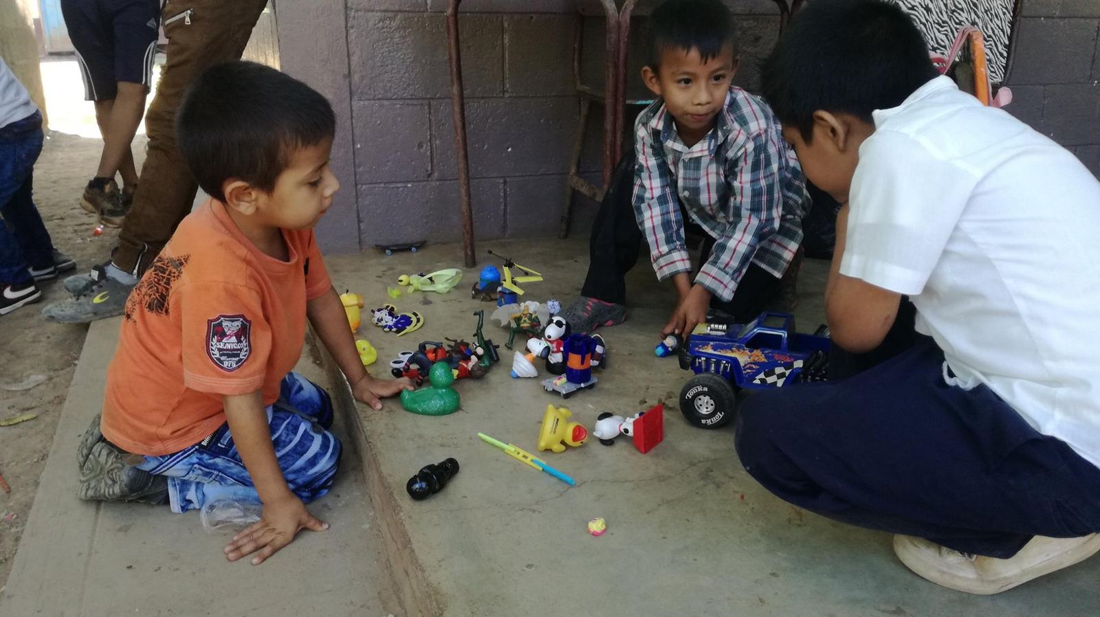 Three boys play on a concrete floor with rubber ducks, figurines and a toy truck
