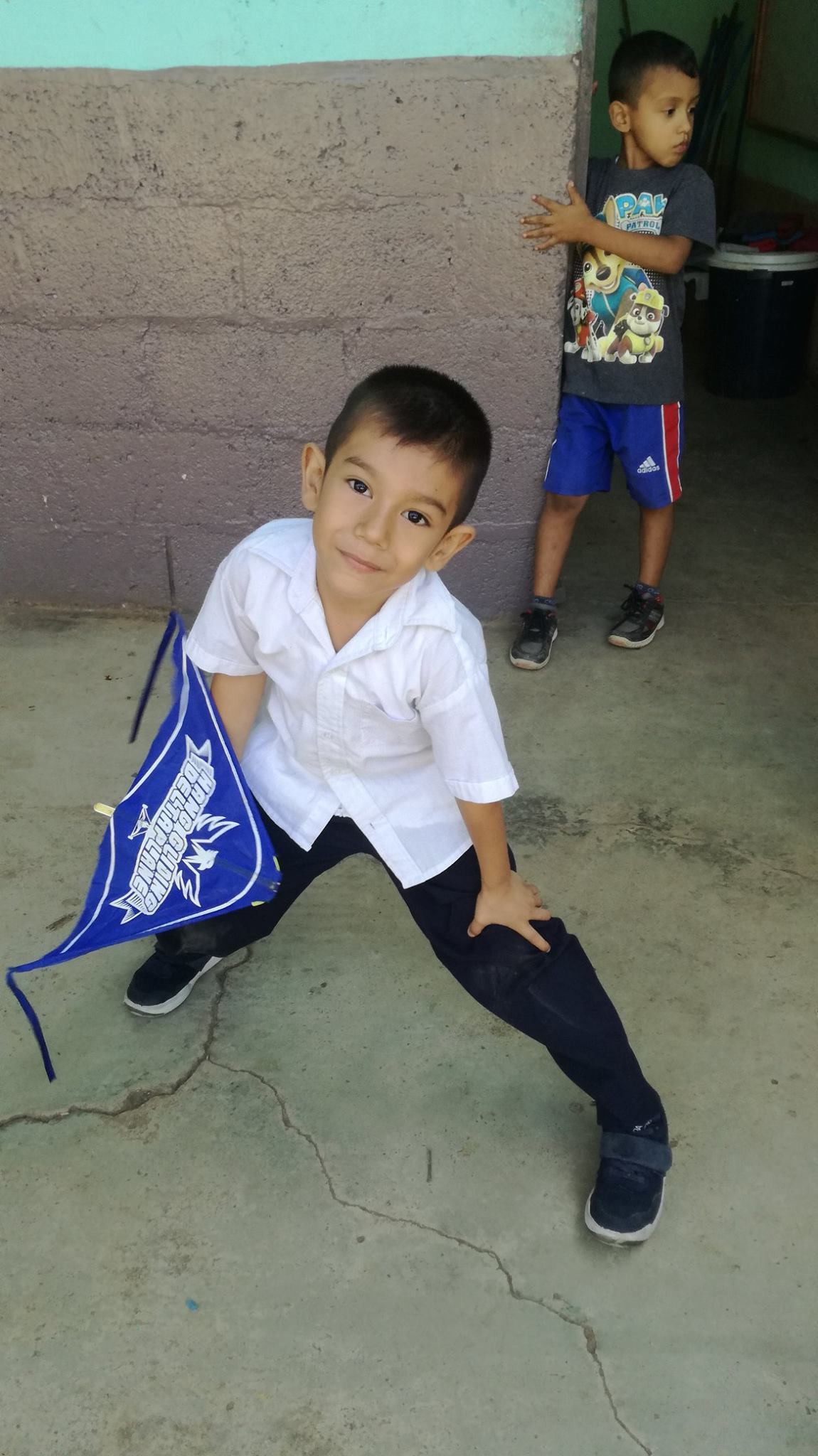 A young schoolboy in uniform strikes a pose and smiles, holding a blue kite