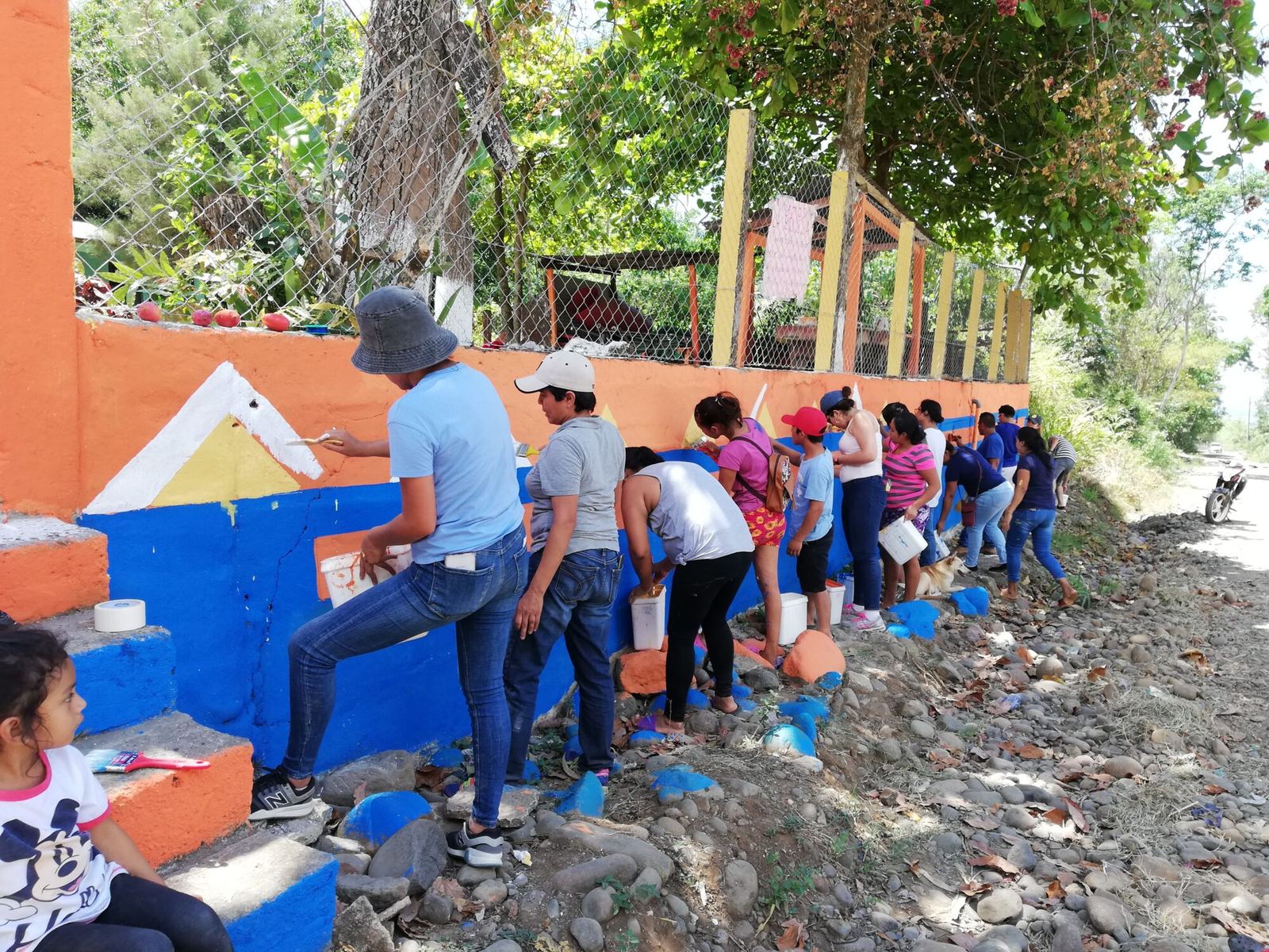Volunteers and children paint the school’s outer wall with colorful triangles on orange and blue
