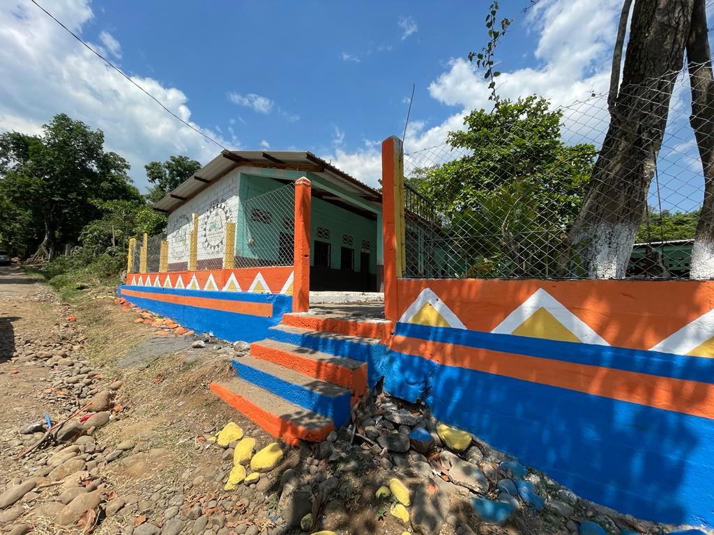 A rural school with its wall, entrance steps and stones painted orange, blue, white and yellow