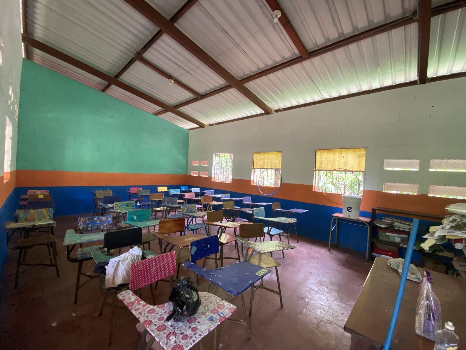 A classroom freshly painted green, white, orange and blue, with neatly arranged desks covered in bright paper