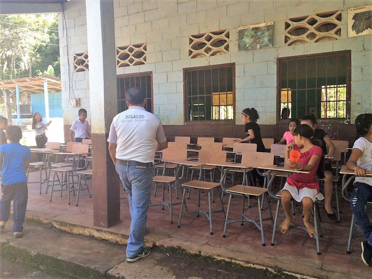 New wooden desks in the corridor of the Las Delicias school, with girls seated and a teacher seen from behind