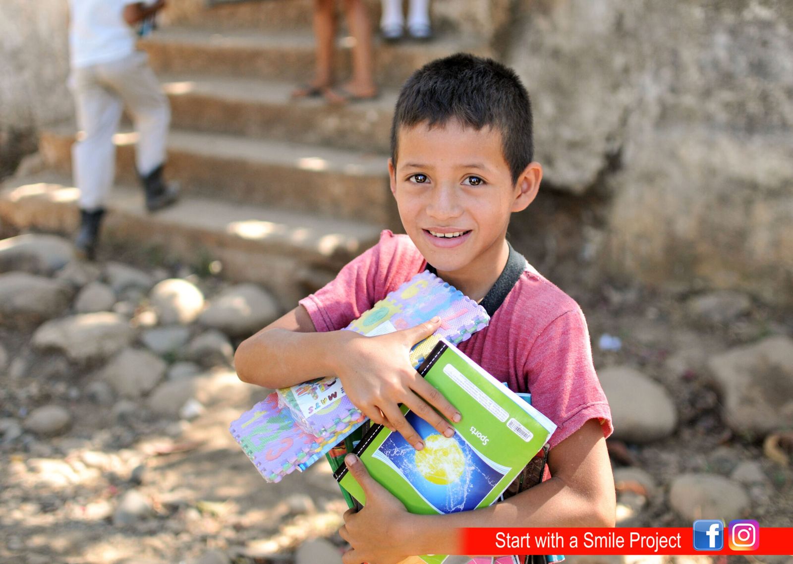 A smiling boy hugs new notebooks and a pack of foam letter tiles during a school supplies handout