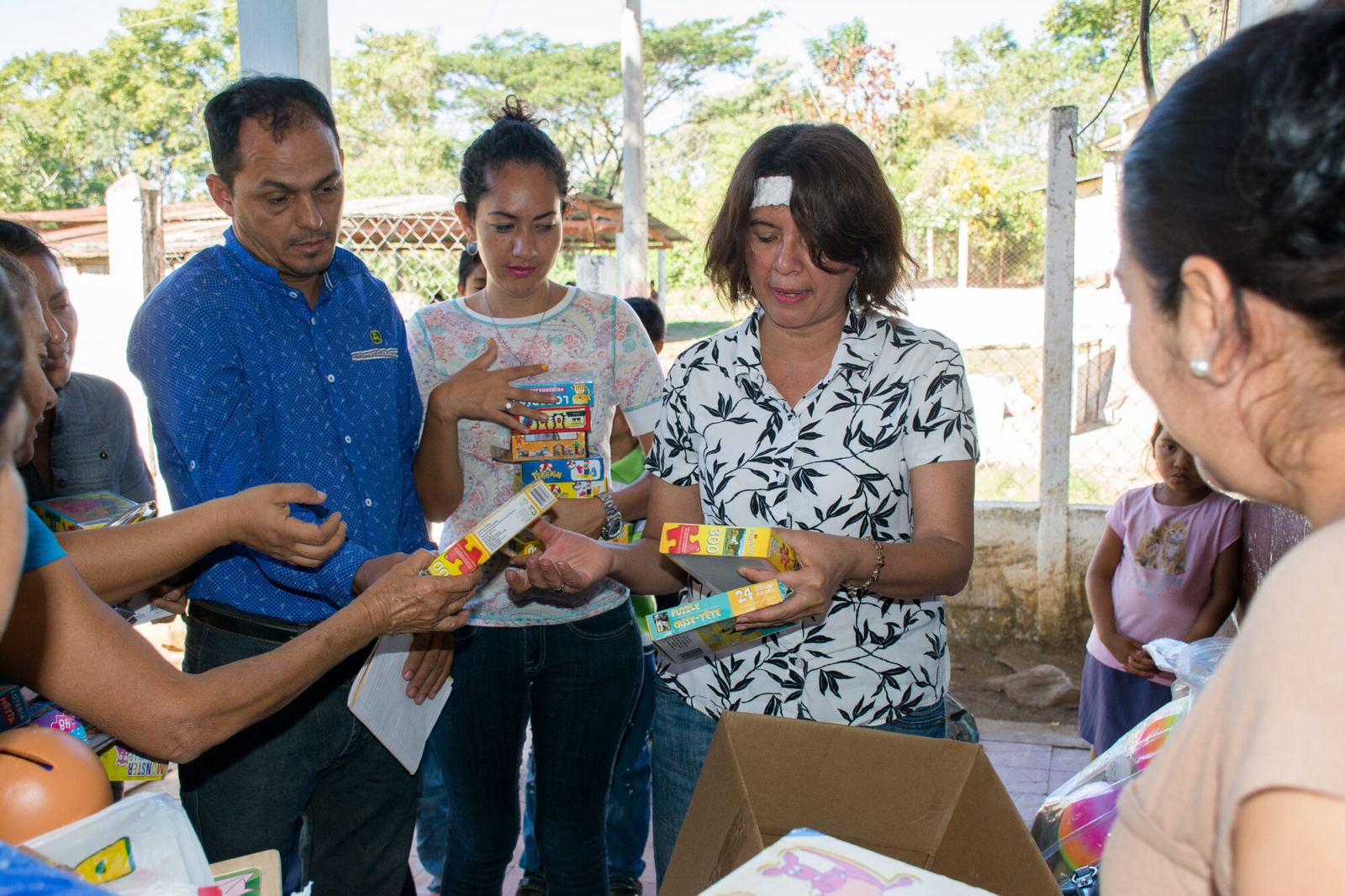 Adults hand out puzzles and toys from a cardboard box as a young girl watches in the background