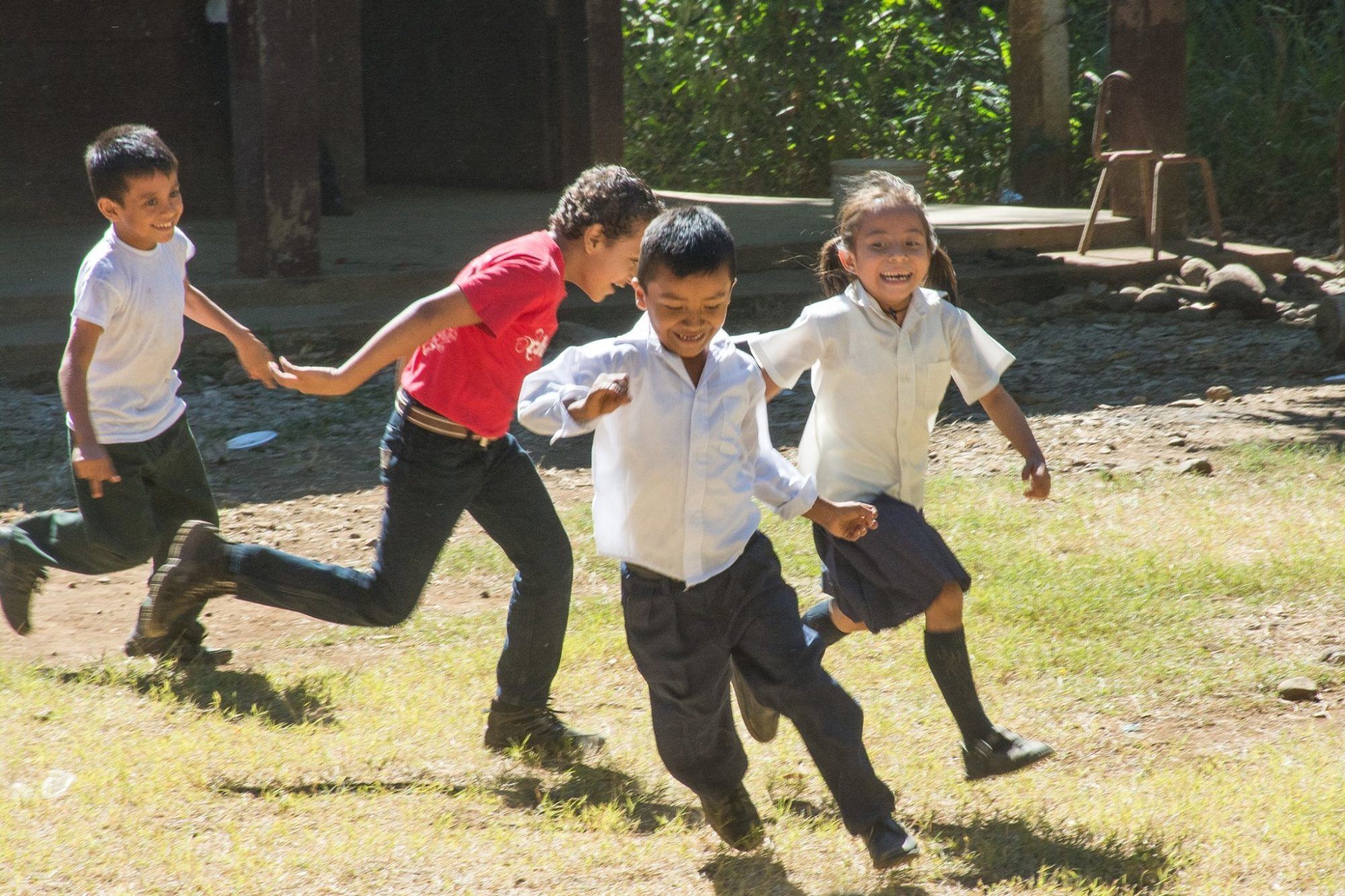 Four children run hand in hand, laughing, across a sunny schoolyard