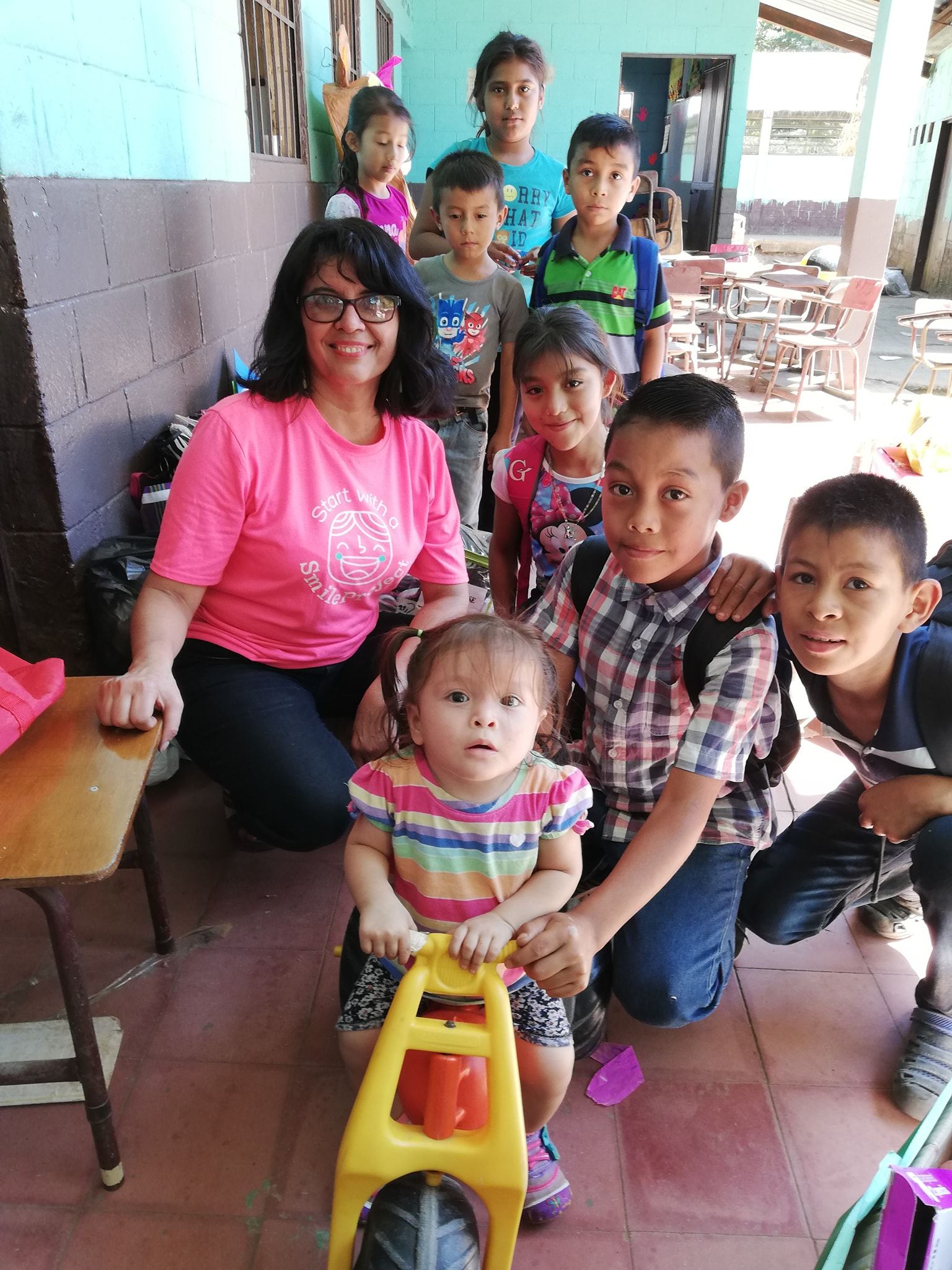 Amalia, in a pink project T-shirt, crouches surrounded by schoolchildren