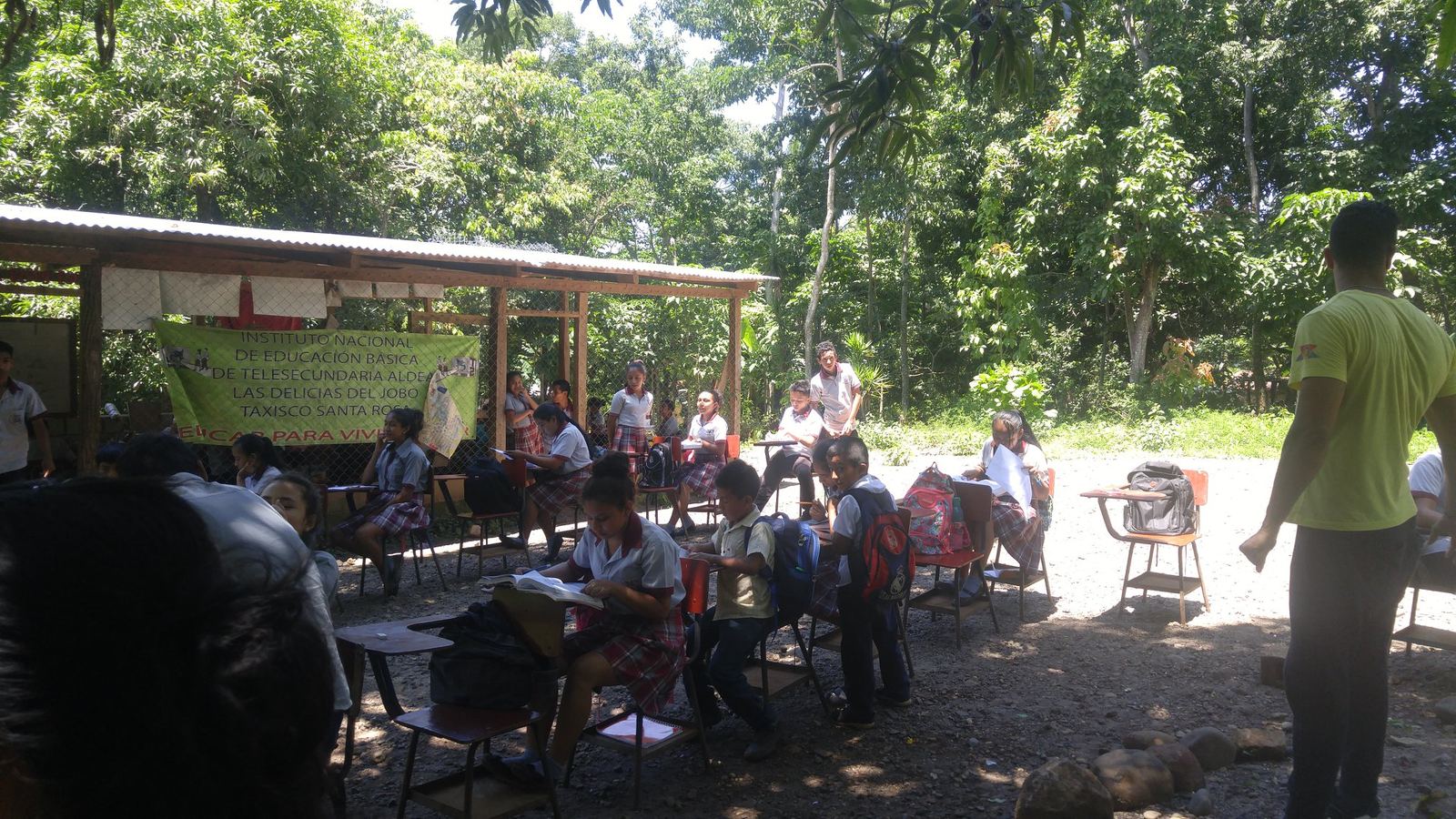 Uniformed students work at outdoor desks beside the open-air shelter of the Telesecundaria in Las Delicias del Jobo
