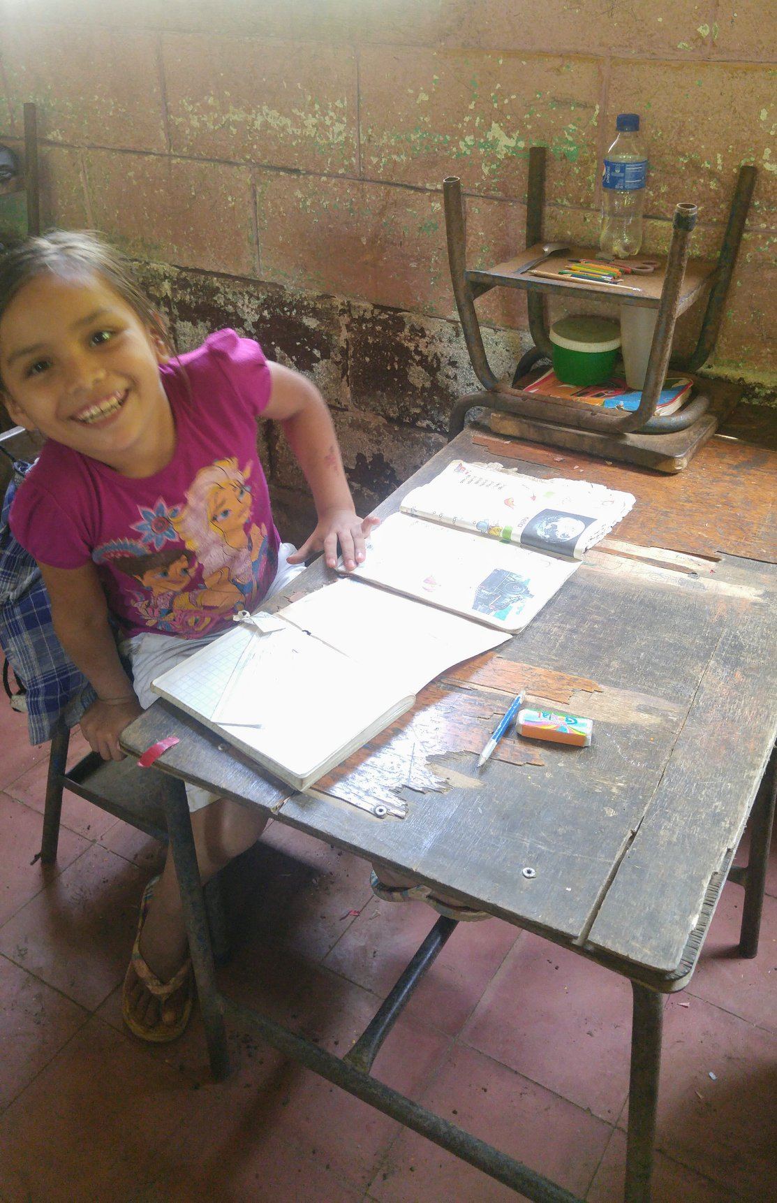 A girl smiles at her wooden desk with her open notebook, a pen and an eraser