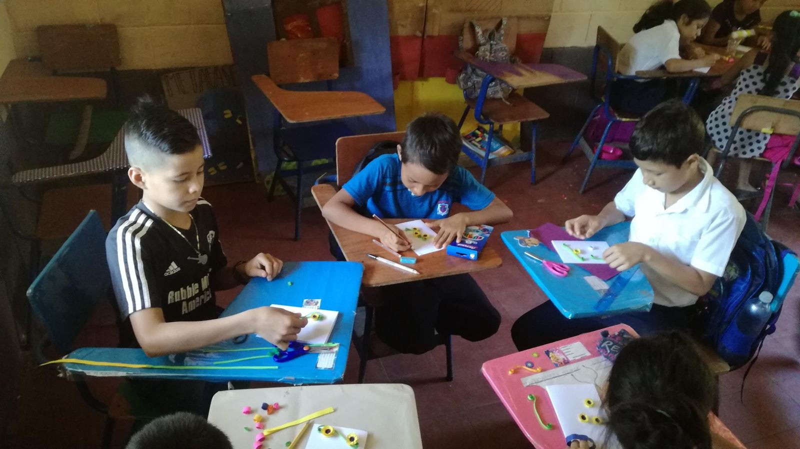 Children make cards with rolled paper-strip flowers at their colorful classroom desks