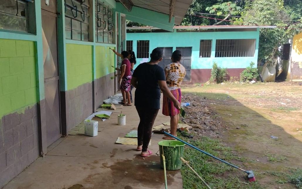 Women paint the outside walls of school classrooms green with rollers and paint trays