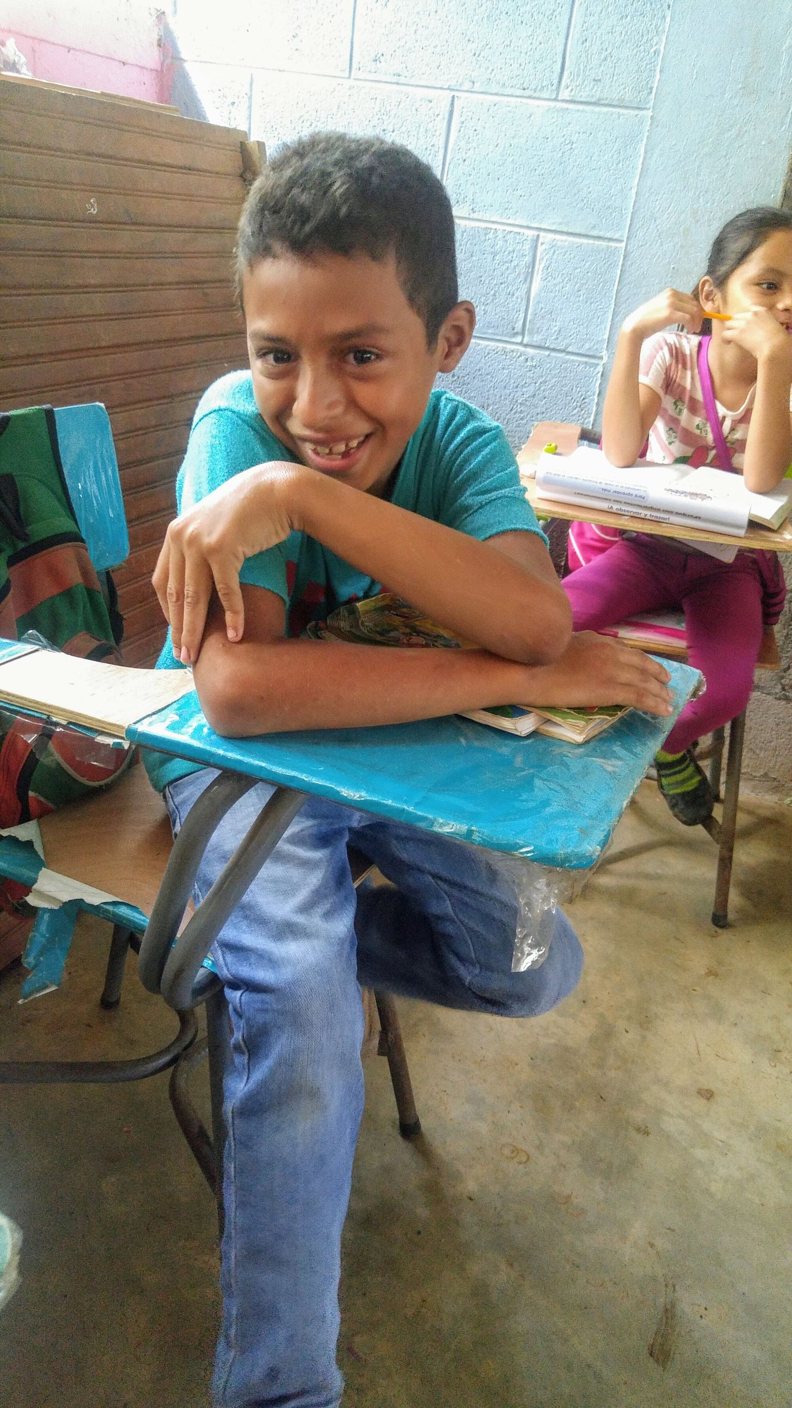 A boy laughs as he leans on his desk, arms folded over his notebooks