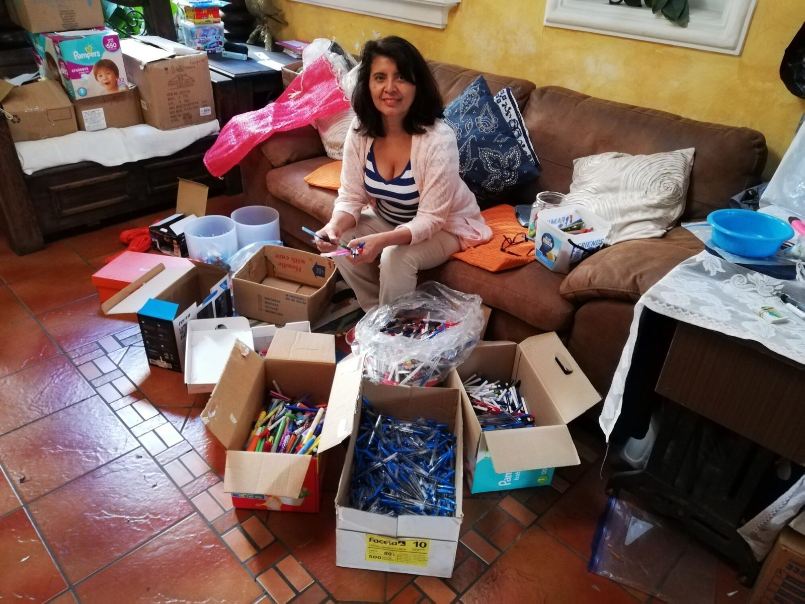 Amalia sorts boxes of donated pens and school supplies in a living room