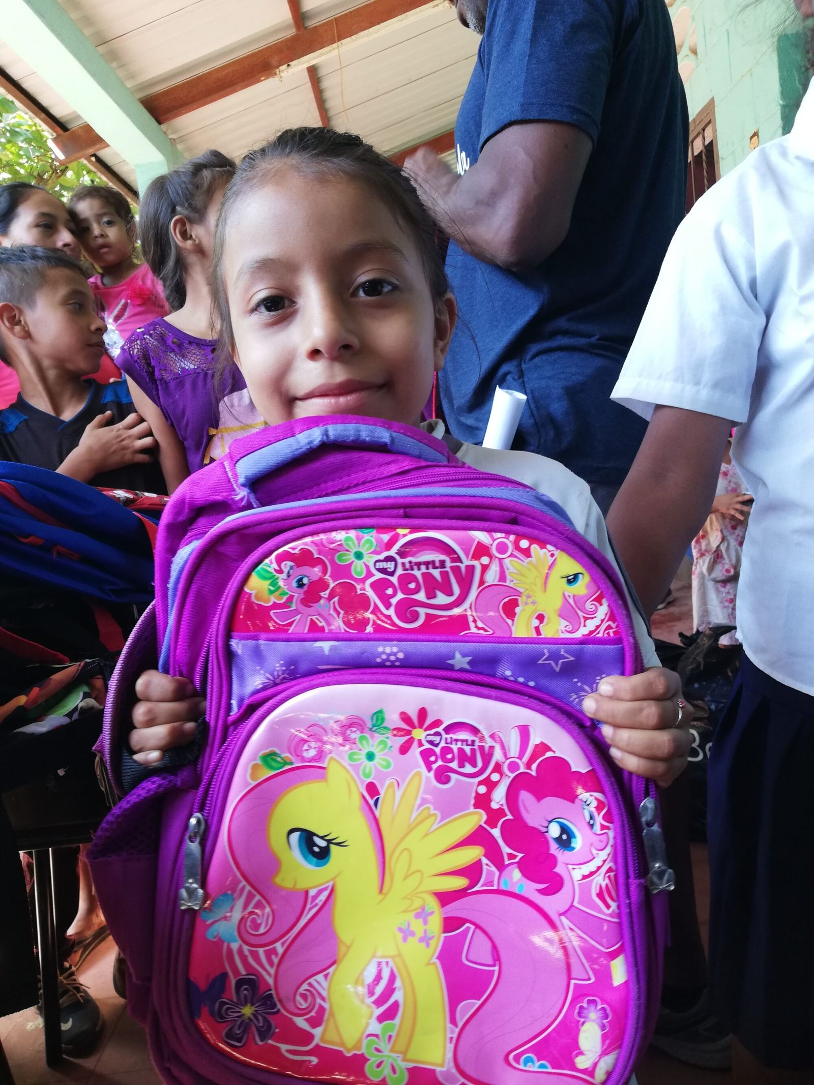 A girl holds up her new My Little Pony backpack in the school corridor