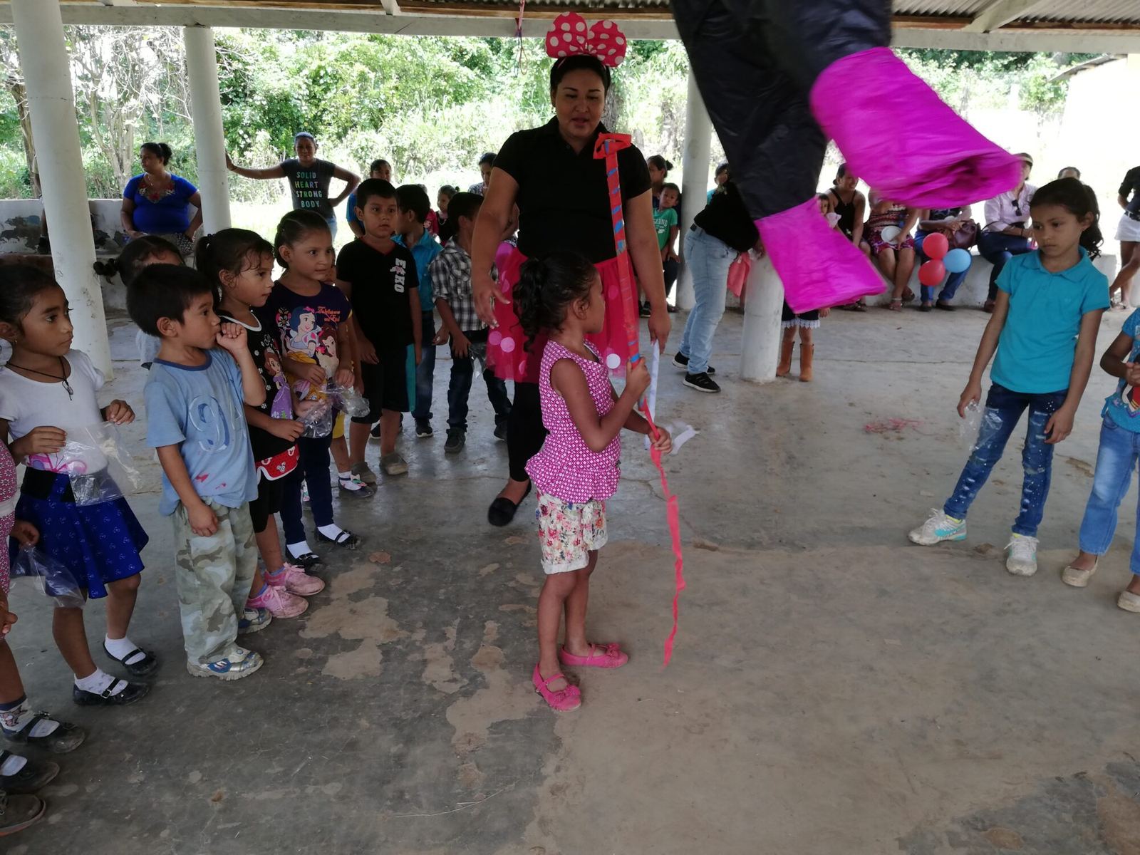 A little girl holds a stick, ready to swing at the piñata, as other children wait their turn