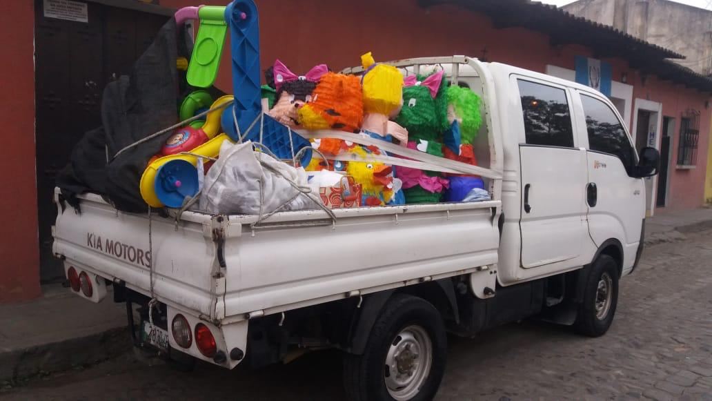 White pickup truck loaded with piñatas and plastic toys, parked on a cobblestone street