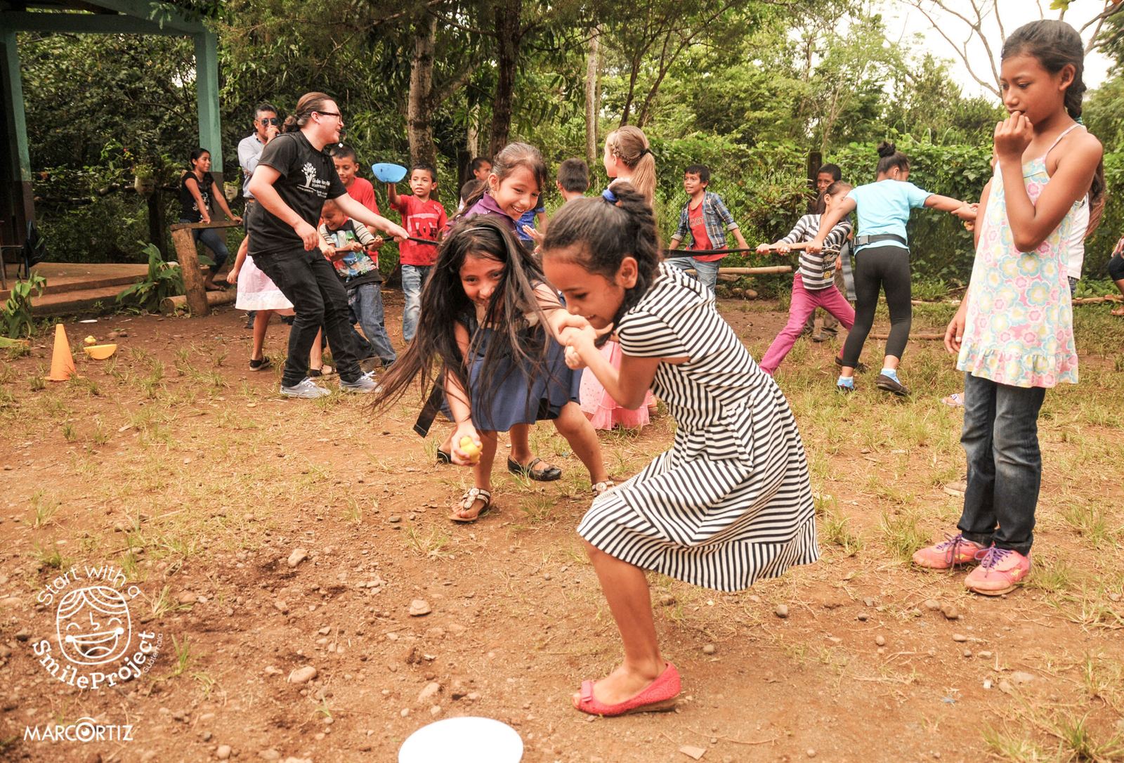 Children play a team game with a rope, small balls and cones on a dirt field during Children’s Day
