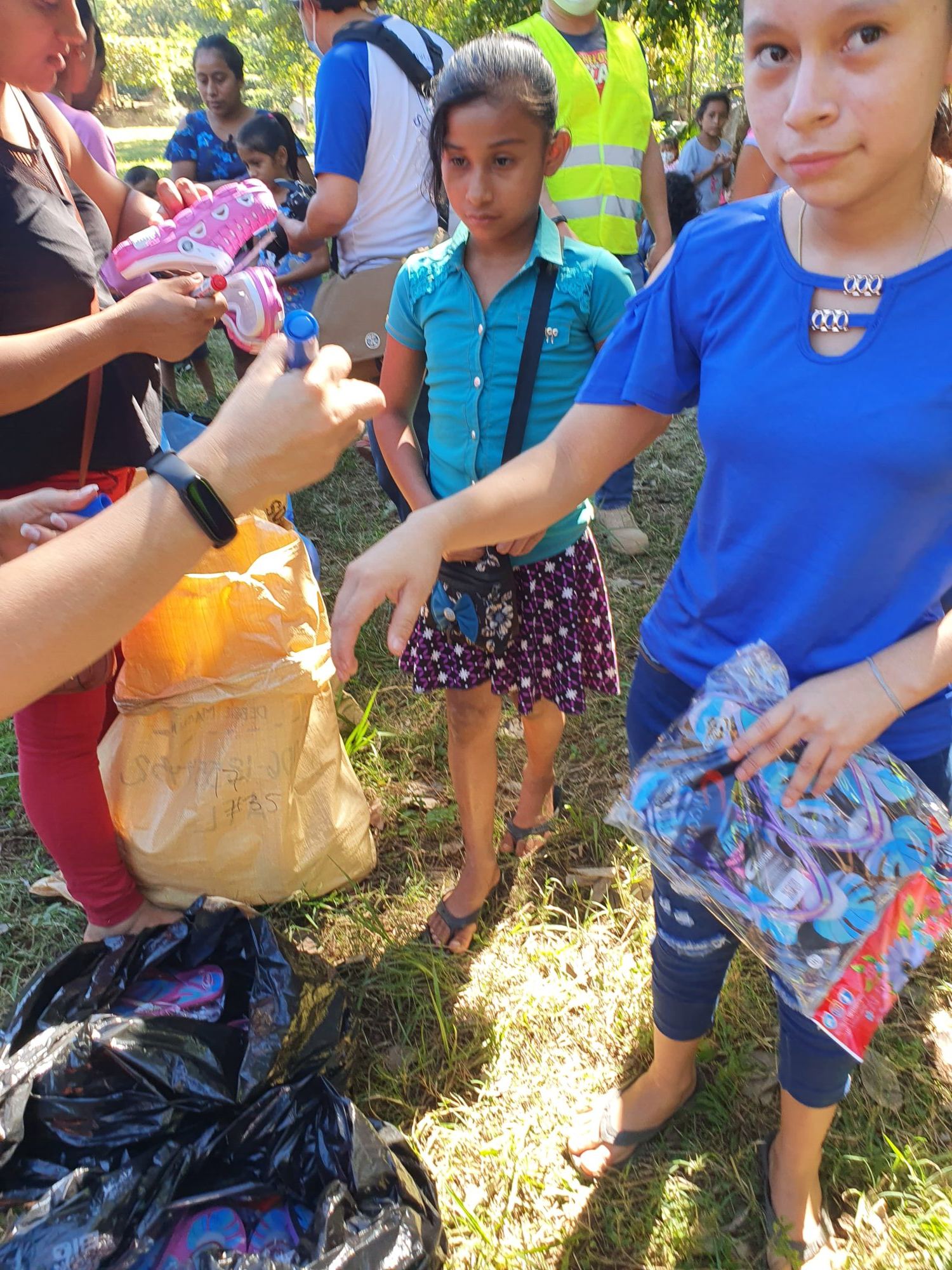 Outdoor sandal handout: a girl waits beside a sack and bags full of footwear
