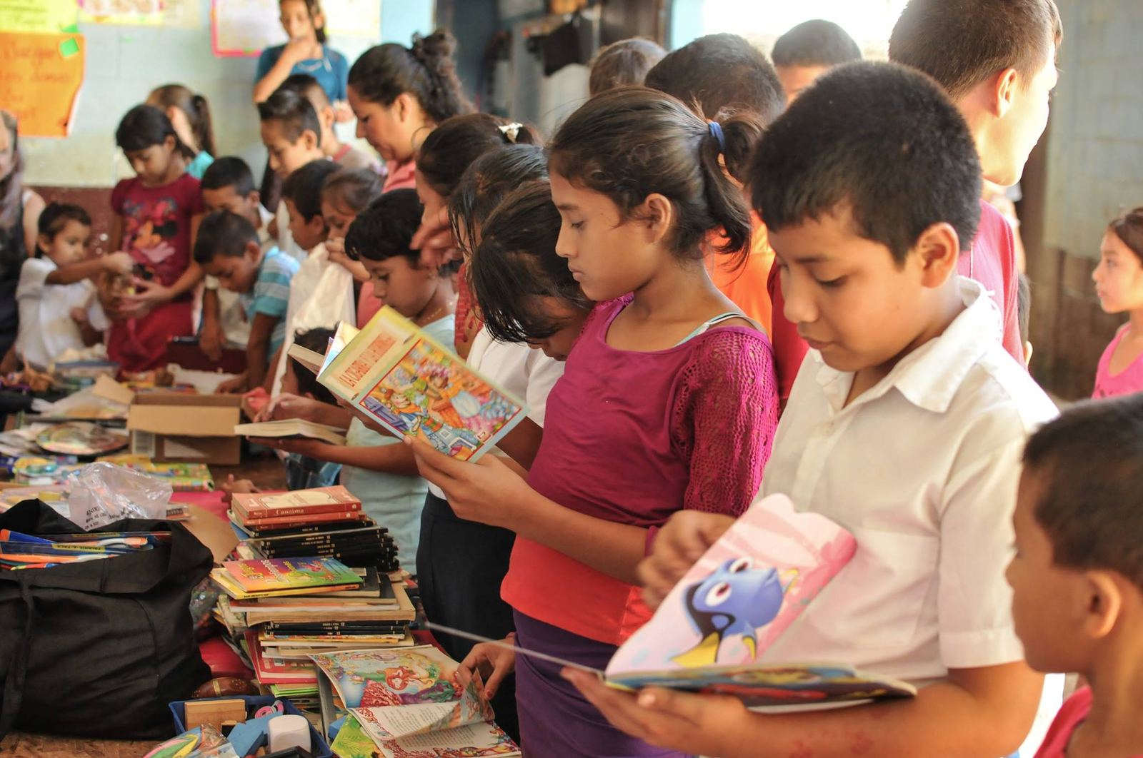 Children browse donated storybooks piled on a table at their school in Las Delicias del Jobo