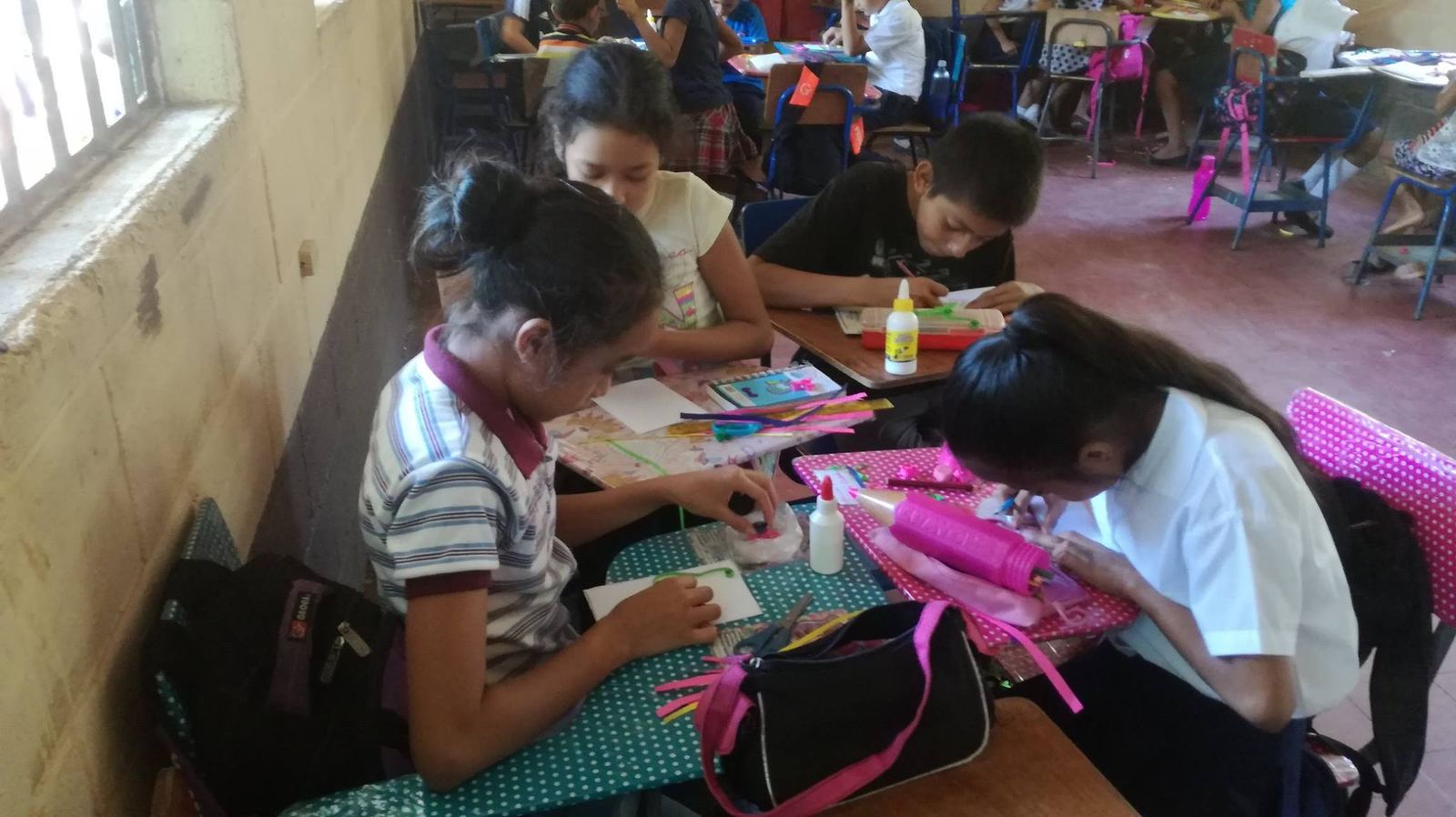 Students make crafts with pipe cleaners, cards and glue at desks covered in polka-dot paper