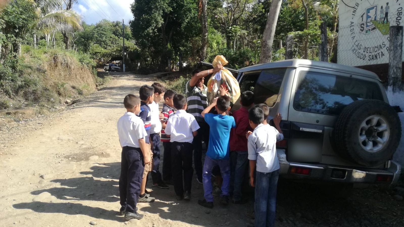 Boys in school uniforms help unload donation sacks from an SUV outside their school