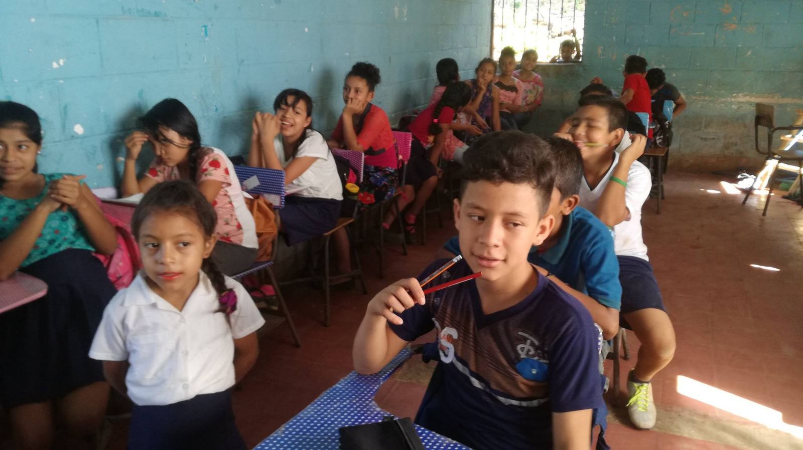 Students of different ages sit at their desks in a classroom with light-blue walls