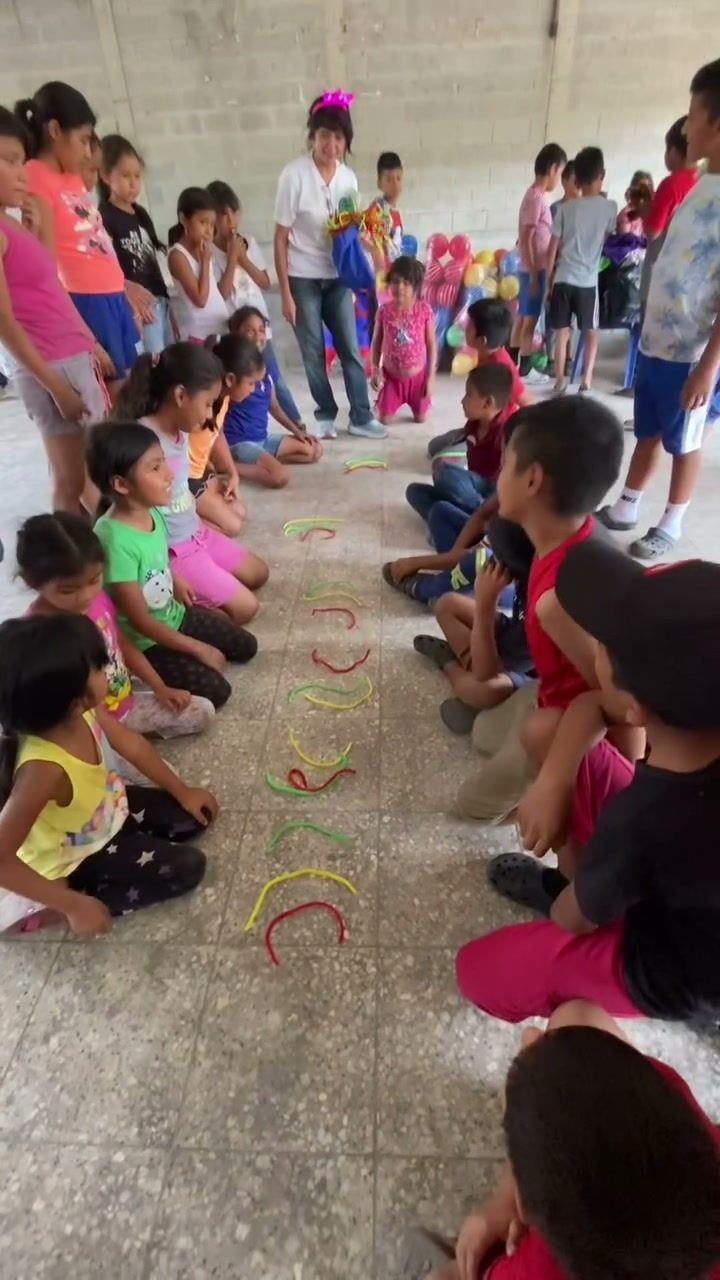 Children sit in two facing rows for a game with colored strips in a hall