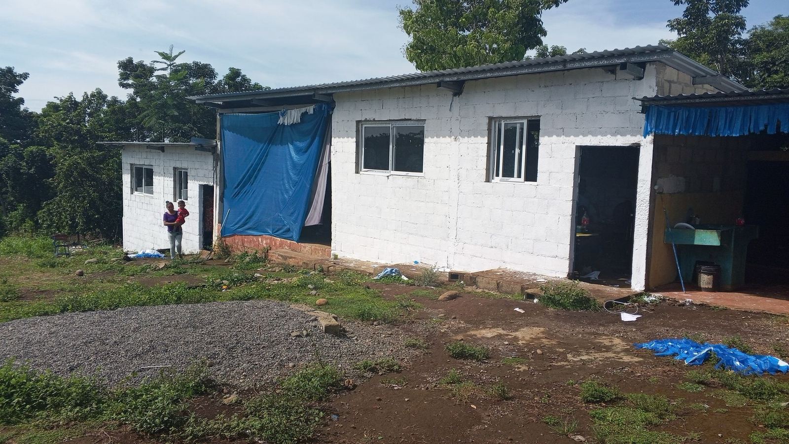 A small white block school with a metal roof and blue tarps in Las Delicias del Jobo, Taxisco