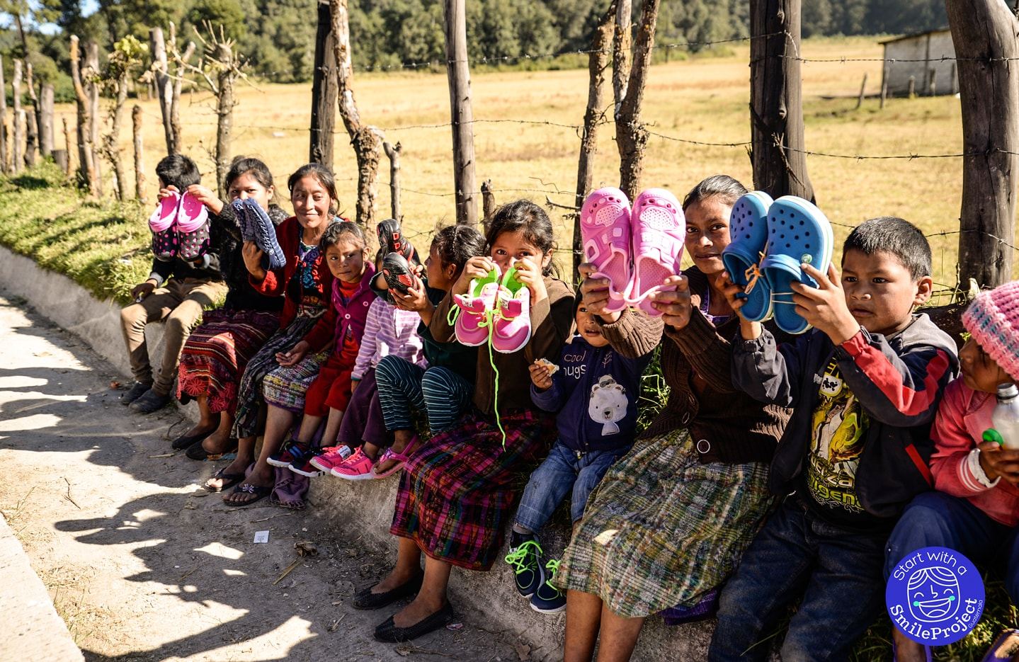 Women and children sitting by the roadside hold up the new shoes they received for Christmas