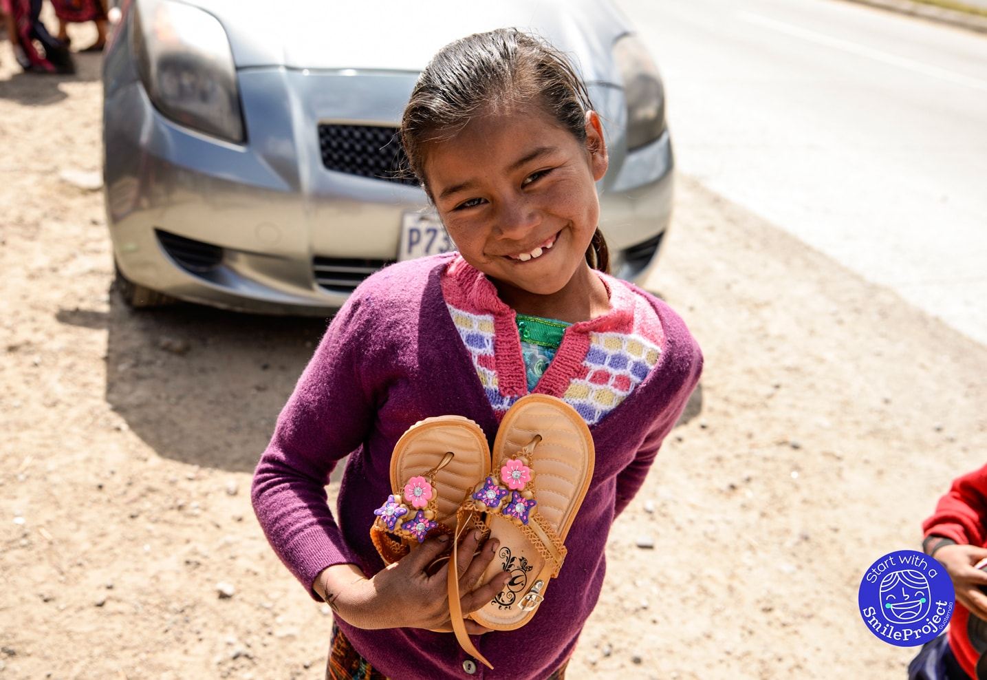 A smiling girl shows her new flowered sandals by the side of the road
