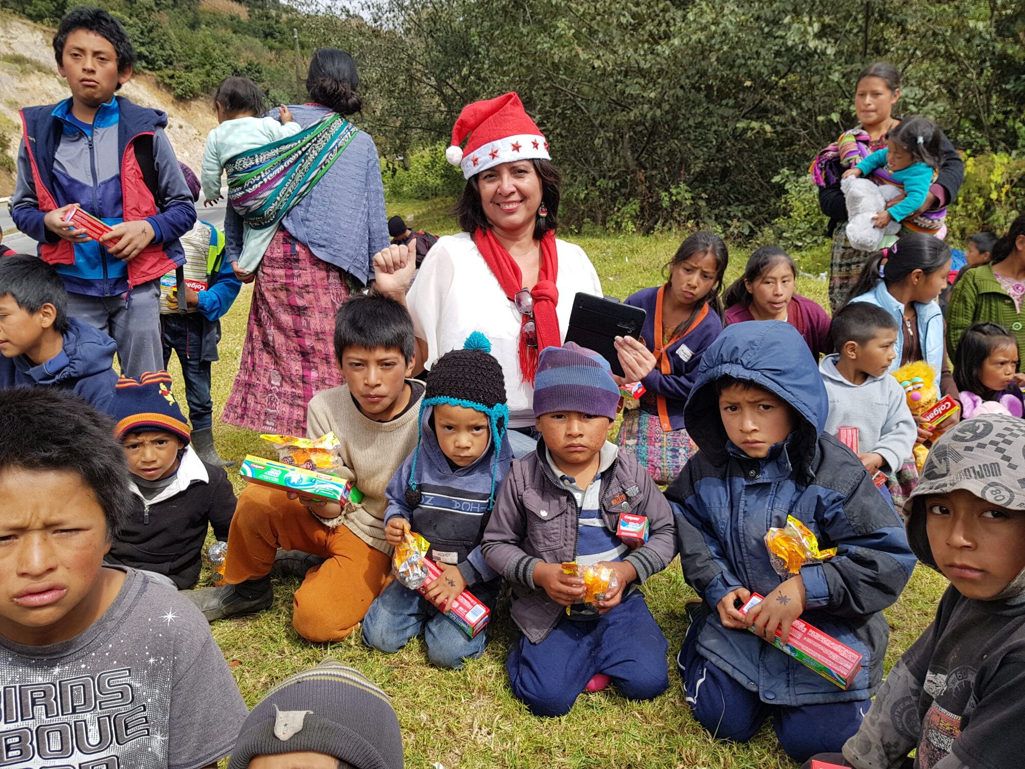 Amalia, in a Santa hat, among children and mothers receiving Christmas gifts by the roadside