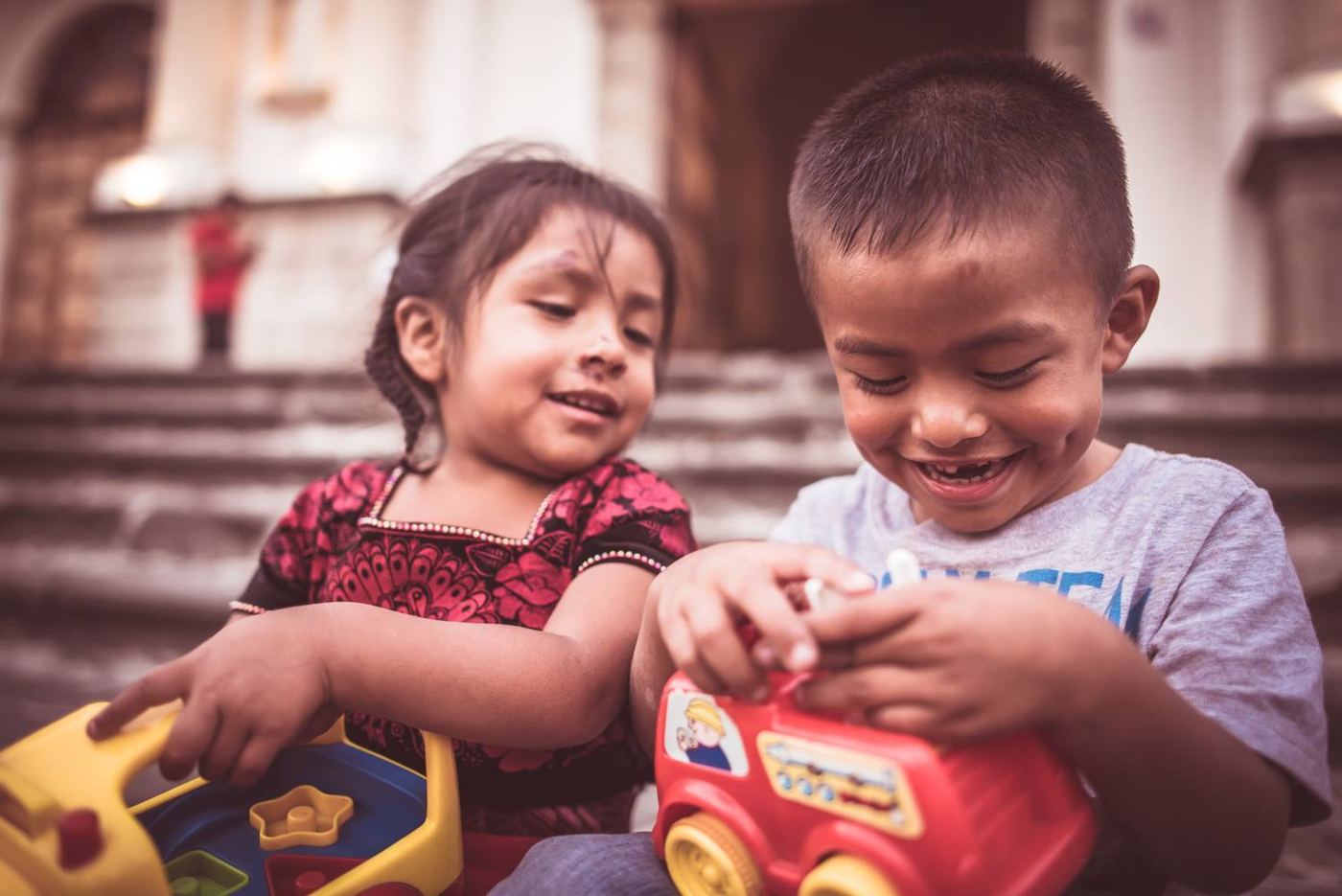Dos niños ríen mientras juegan con sus juguetes nuevos en las gradas de una iglesia de Guatemala